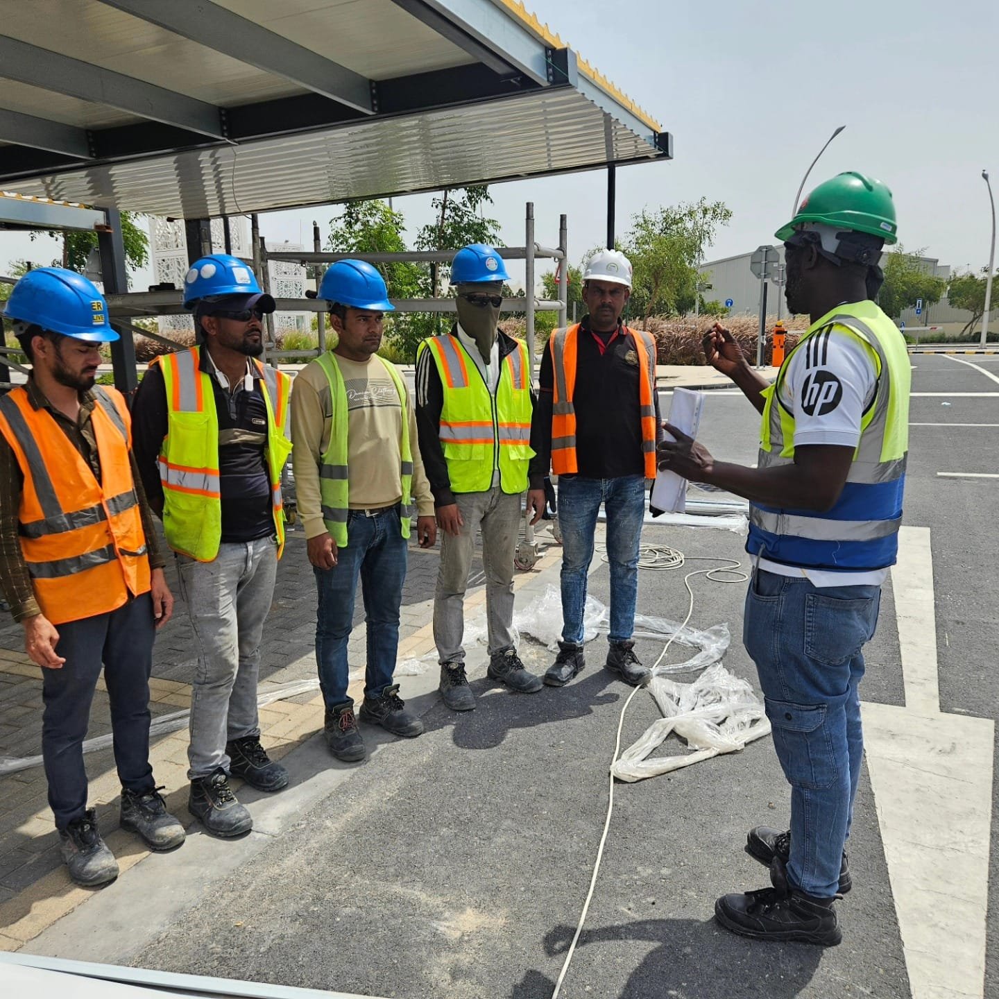 Austin conducting a site safety briefing with a clipboard as workers line up in hi-vis vests