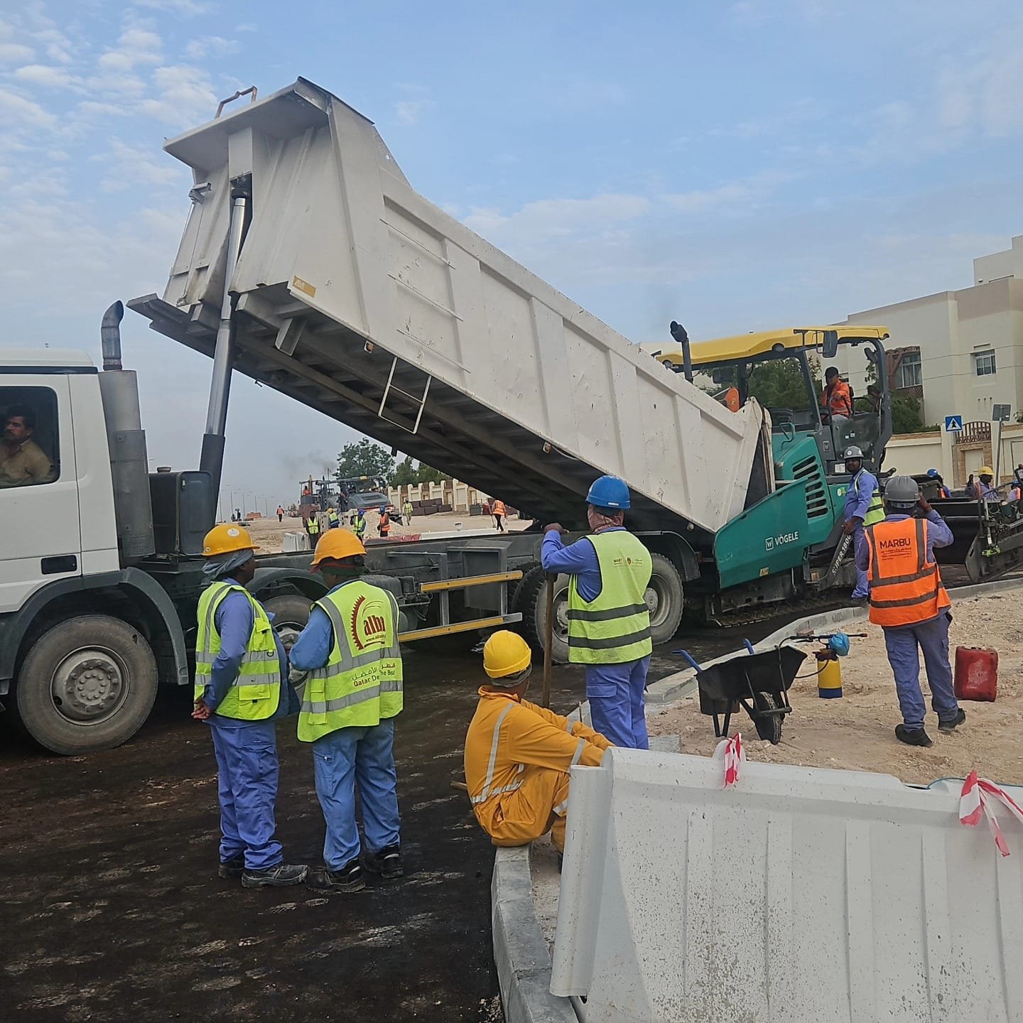 Dump truck tipping material while a hi-vis crew works on a road construction site