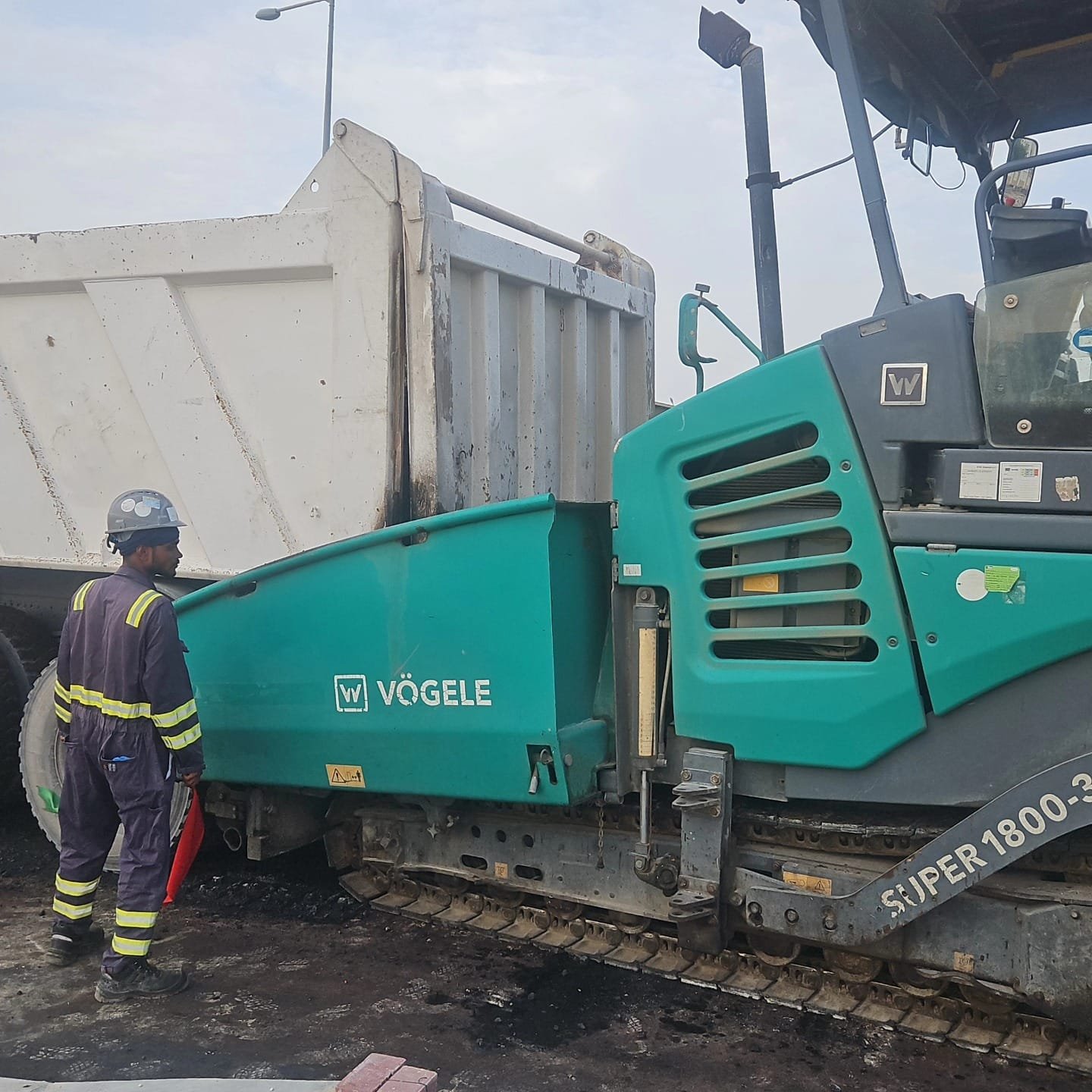 Asphalt paving machine and worker during road construction operations