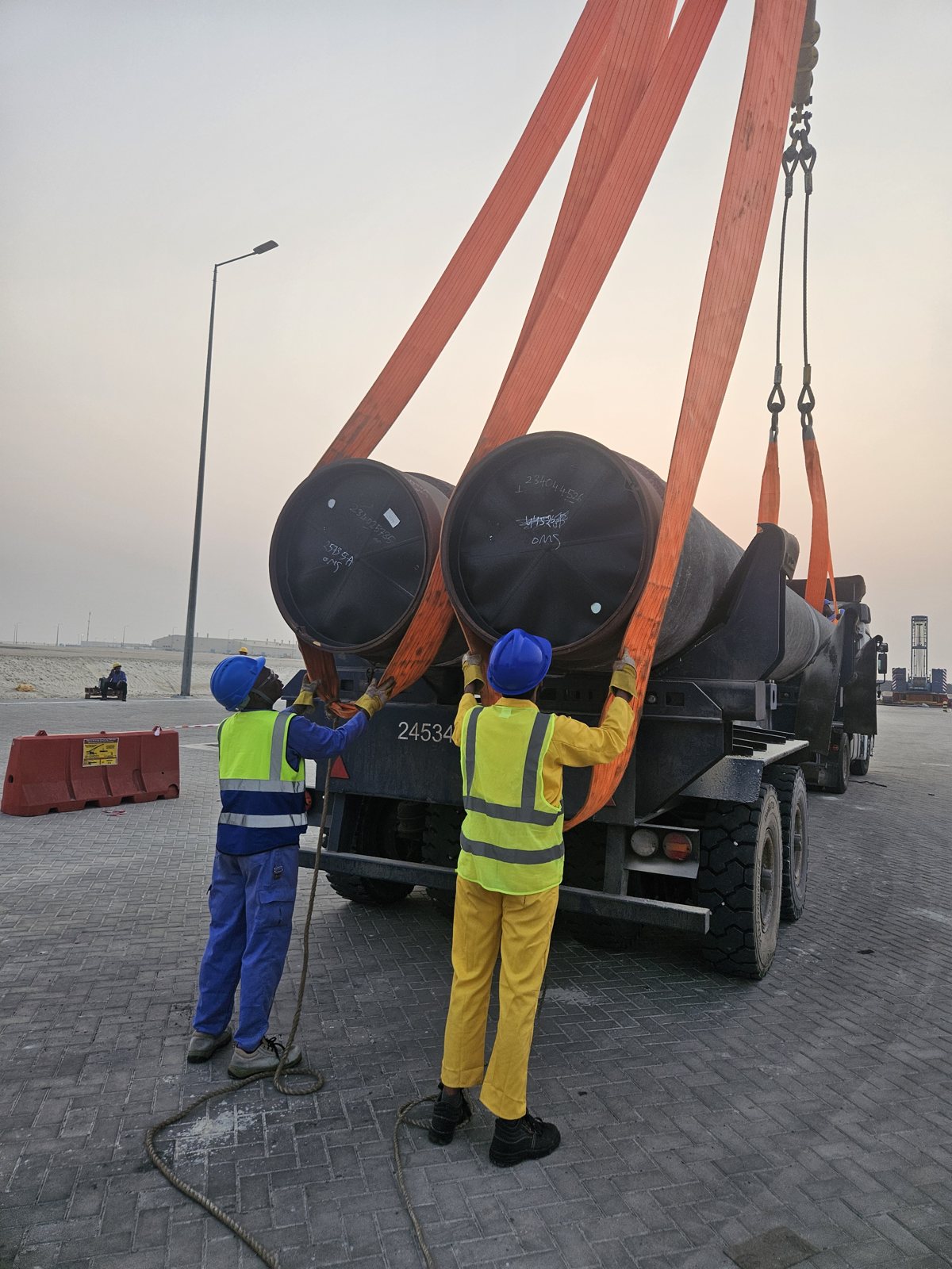 Riggers securing large pipe sections with lifting slings during a heavy-lift operation